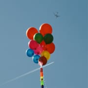 A bright blue sky is filled with an aircraft, balloon, kite, and plane, creating a thrilling atmosphere for outdoor air sports.