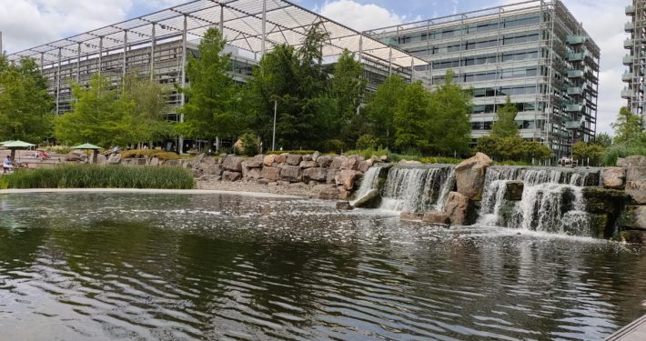 The waterfall cascades over the body of water, with buildings in the background.
